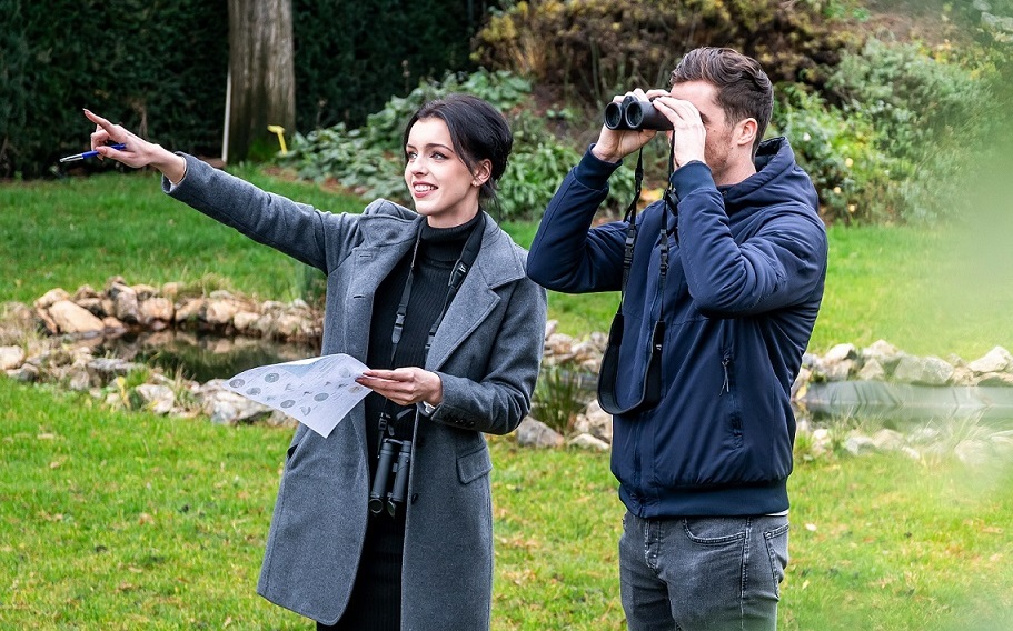 Deux personnes se rencontrent pour observer les oiseaux. L'homme regarde à travers des jumelles, tandis que la femme montre quelque chose du doigt.